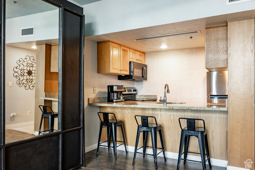 Kitchen with appliances with stainless steel finishes, light brown cabinets, a kitchen bar, and a peninsula