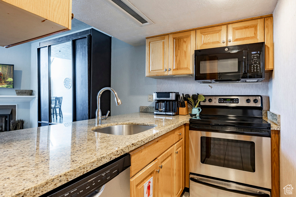 Kitchen with stainless steel appliances, light stone counters, light brown cabinets, and a glass covered fireplace