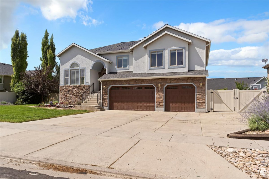 View of front of home featuring a gate, an attached garage, stone siding, concrete driveway, and stucco siding
