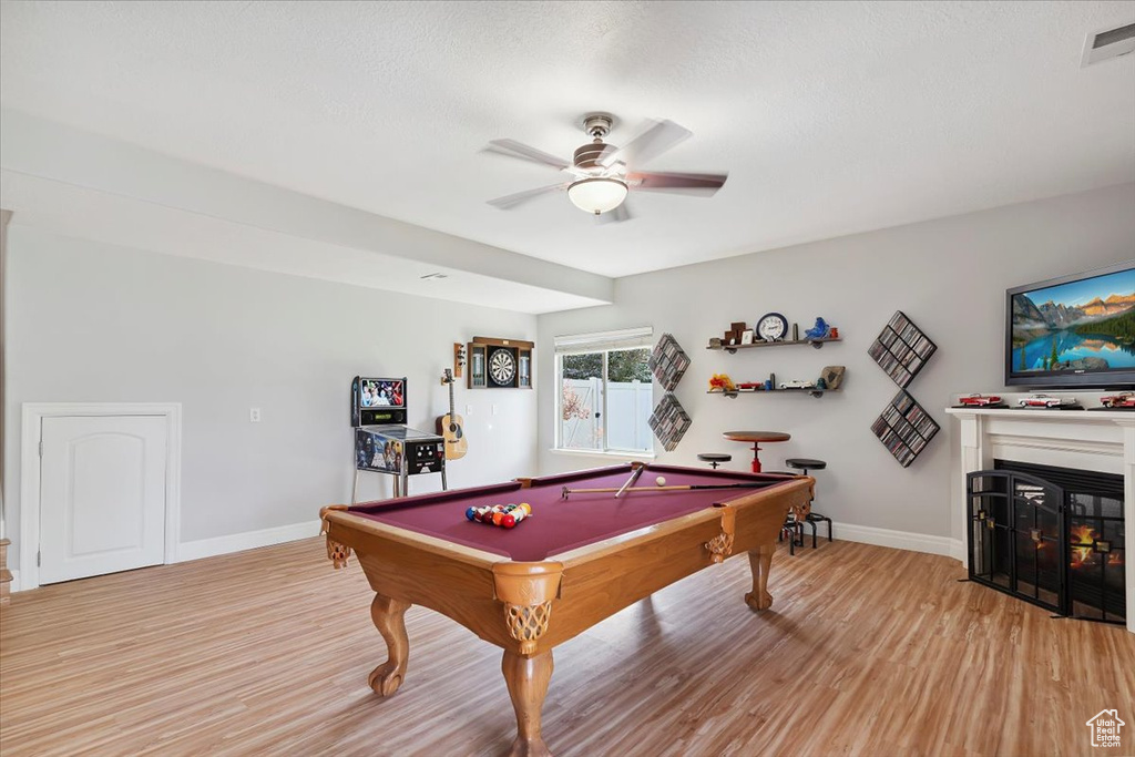 Game room featuring light wood-style floors, a ceiling fan, billiards table, and a glass covered fireplace