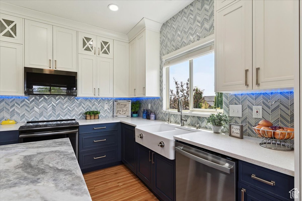 Kitchen featuring stainless steel appliances, white cabinets, blue cabinets, and tasteful backsplash
