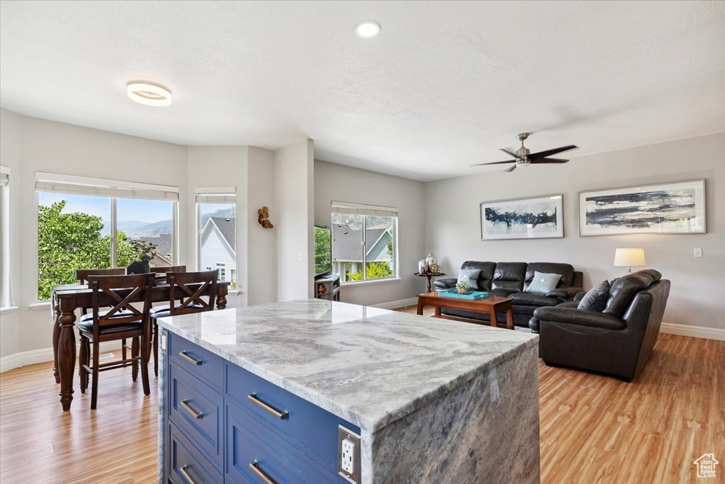 Kitchen featuring blue cabinets, light wood-style flooring, ceiling fan, and light stone counters