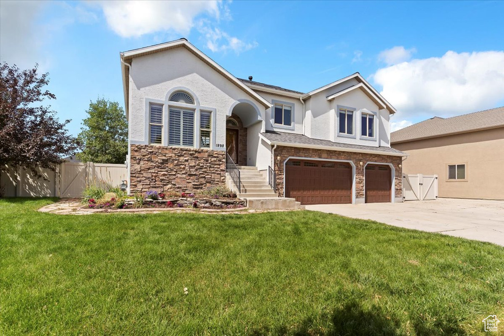 View of front of home with a garage, a gate, stone siding, and driveway