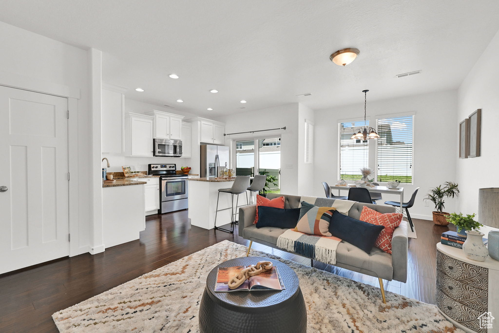 Living room with dark wood-type flooring, a chandelier, and recessed lighting