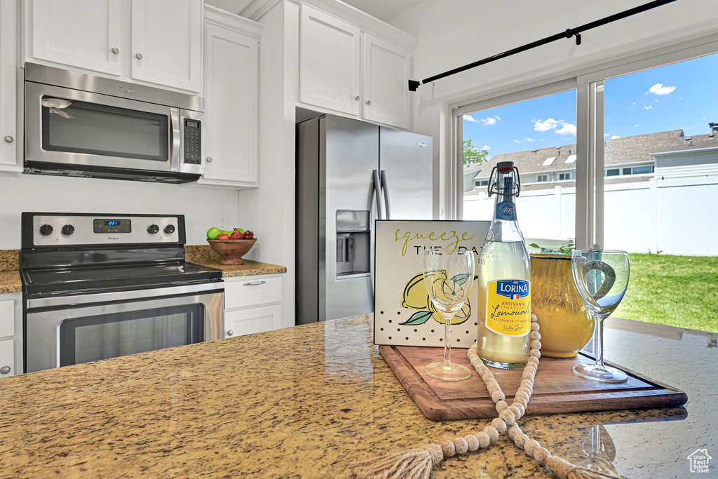 Kitchen featuring stainless steel appliances, white cabinets, and light stone countertops