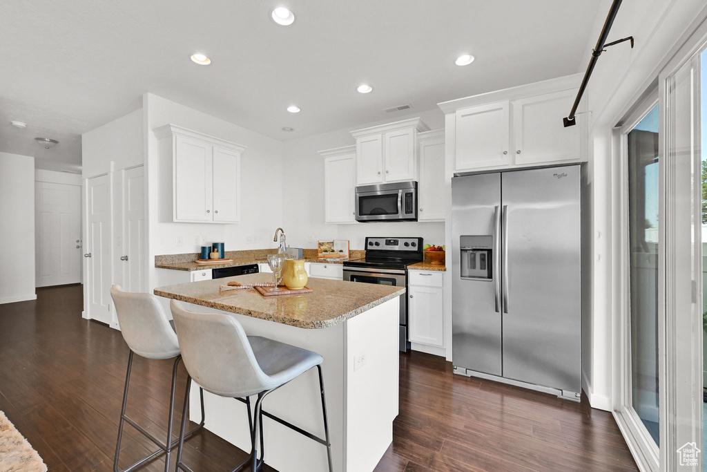 Kitchen featuring stainless steel appliances, dark wood-type flooring, a center island, white cabinets, and a breakfast bar