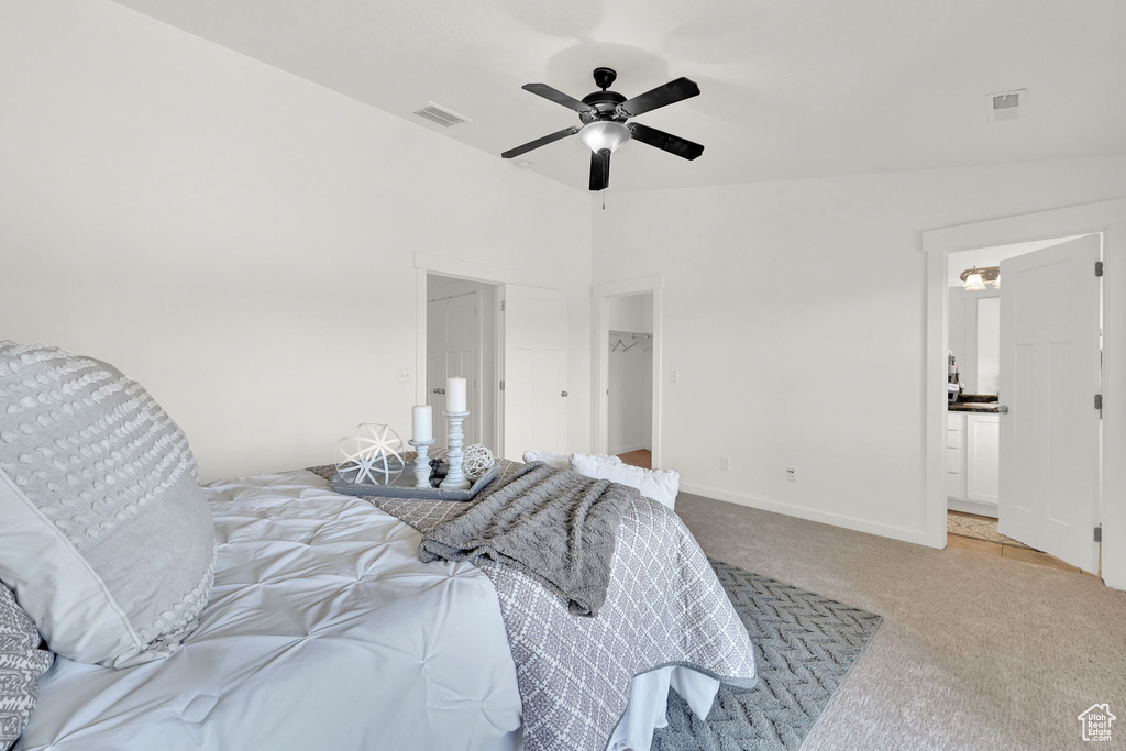 Bedroom featuring light colored carpet, a spacious closet, and ceiling fan