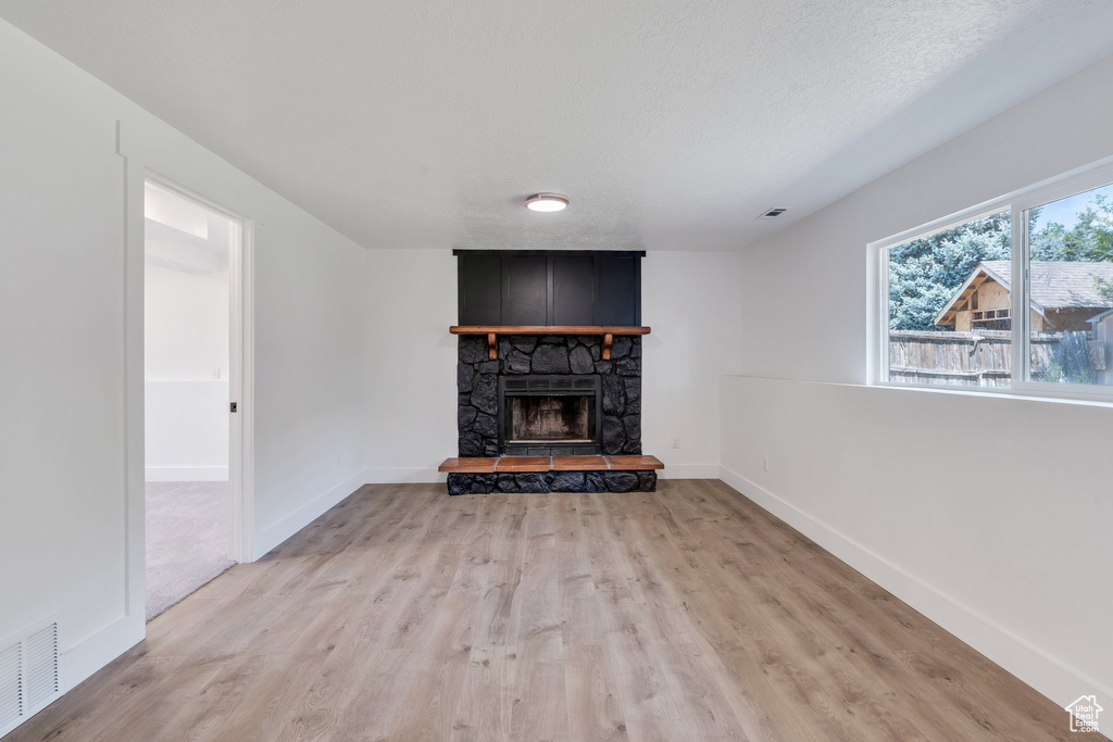 Unfurnished living room with light wood-style flooring and a stone fireplace