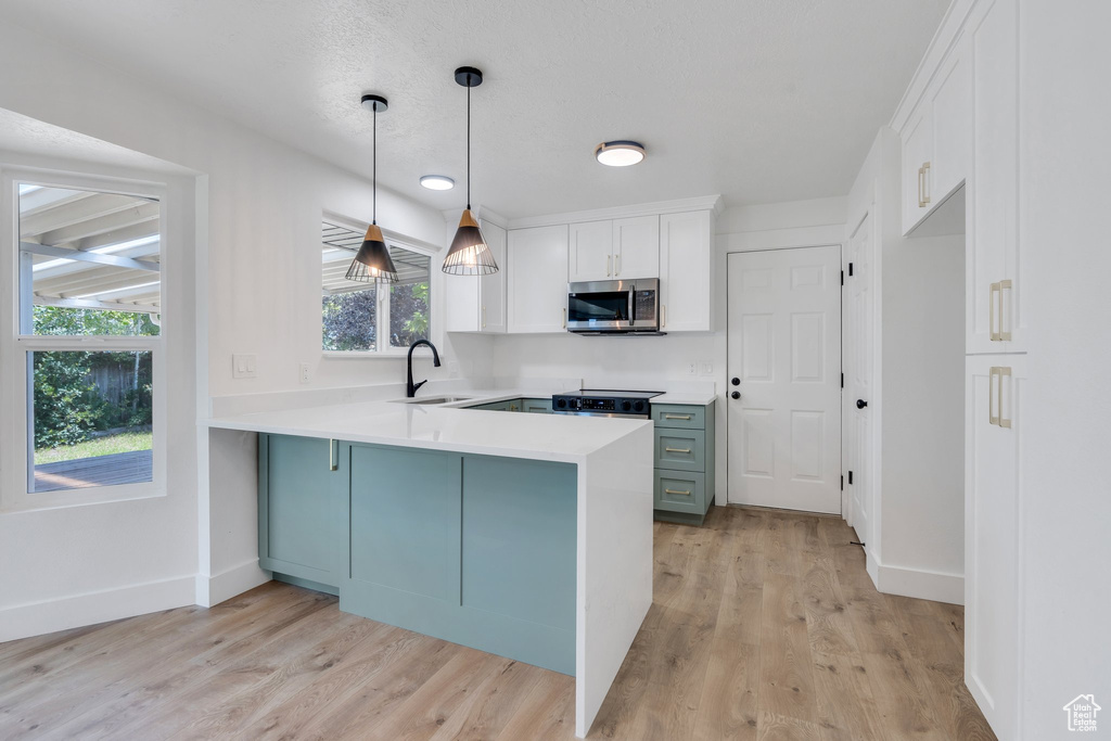 Kitchen with stainless steel microwave, a peninsula, white cabinets, light countertops, and light wood-style floors