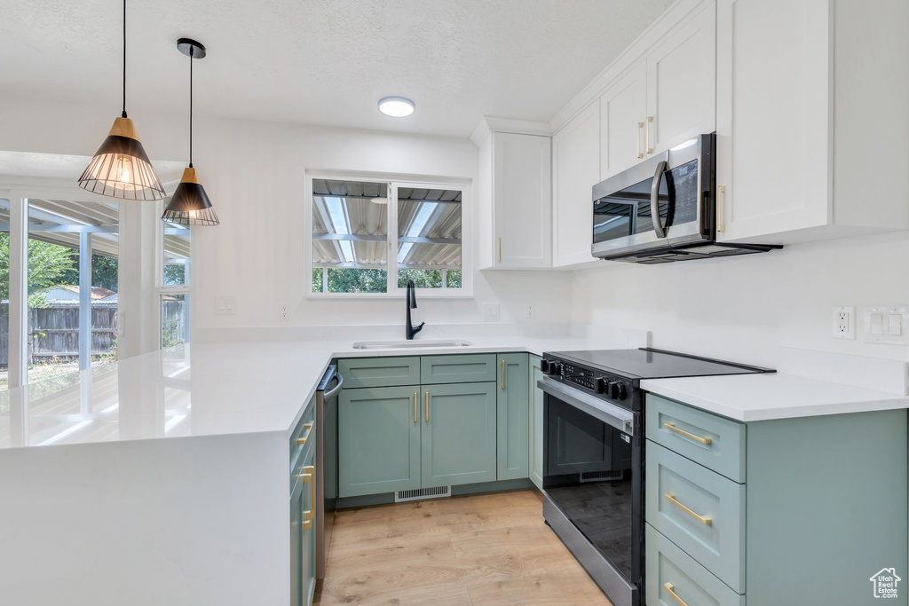 Kitchen with appliances with stainless steel finishes, white cabinets, light wood-type flooring, a peninsula, and green cabinets