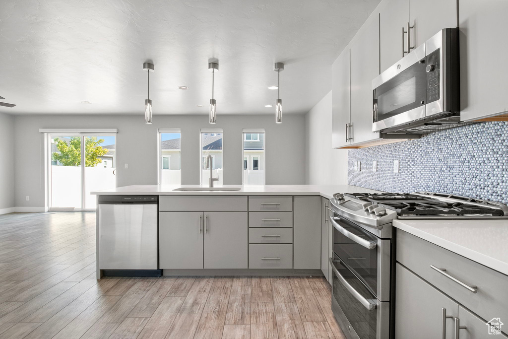 Kitchen with appliances with stainless steel finishes, gray cabinets, a peninsula, and light countertops