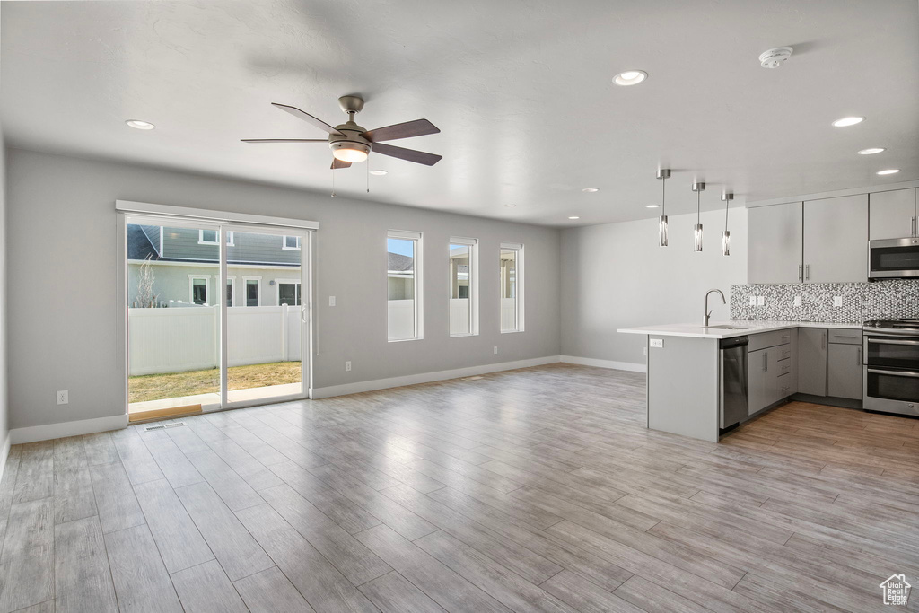 Kitchen featuring appliances with stainless steel finishes, a peninsula, open floor plan, a ceiling fan, and light countertops