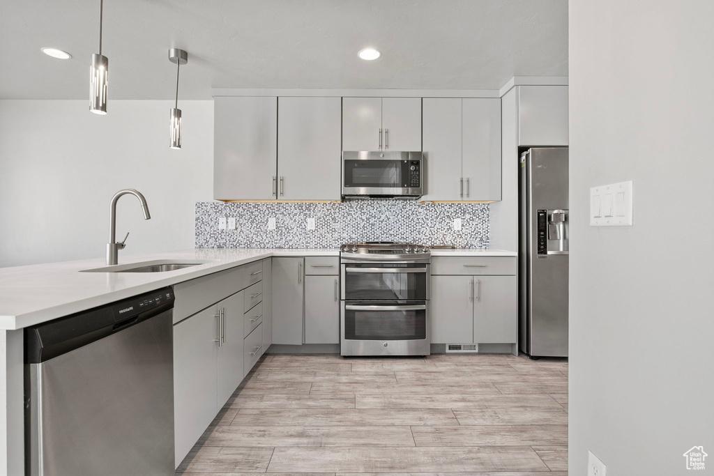 Kitchen featuring appliances with stainless steel finishes, a peninsula, light countertops, hanging light fixtures, and recessed lighting