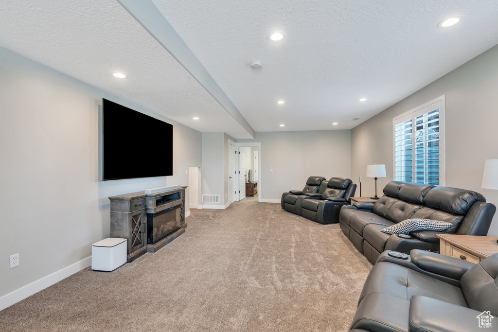 Living area with light colored carpet, recessed lighting, and a glass covered fireplace