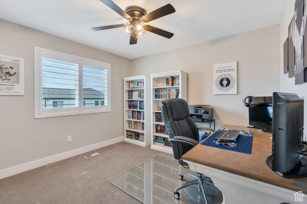 Carpeted home office featuring a ceiling fan and baseboards