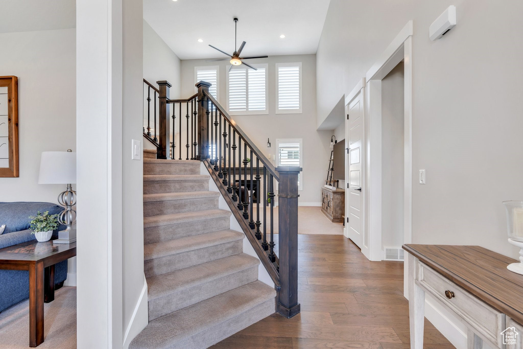 Staircase with a ceiling fan, wood finished floors, recessed lighting, and a towering ceiling