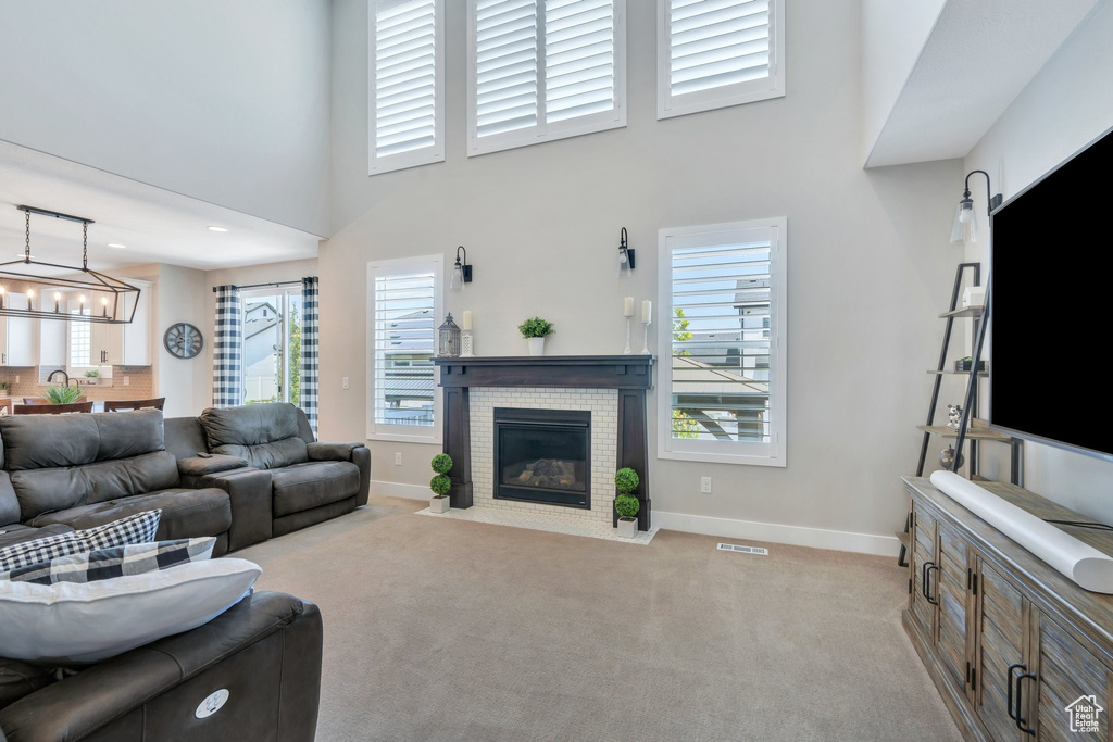 Living area with light carpet, a fireplace, a high ceiling, and a chandelier