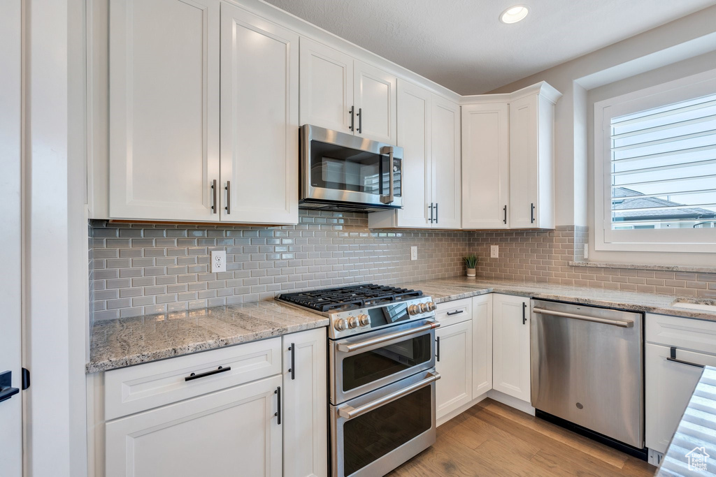 Kitchen featuring appliances with stainless steel finishes, white cabinetry, light wood-style flooring, decorative backsplash, and recessed lighting