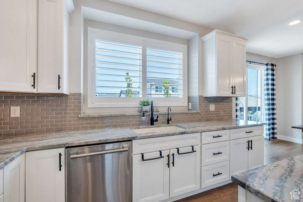 Kitchen featuring dishwasher, wood finished floors, white cabinets, decorative backsplash, and light stone countertops