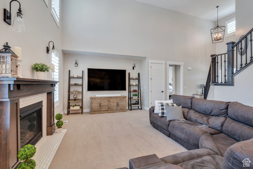 Living area with a high ceiling, a glass covered fireplace, a chandelier, light carpet, and stairs