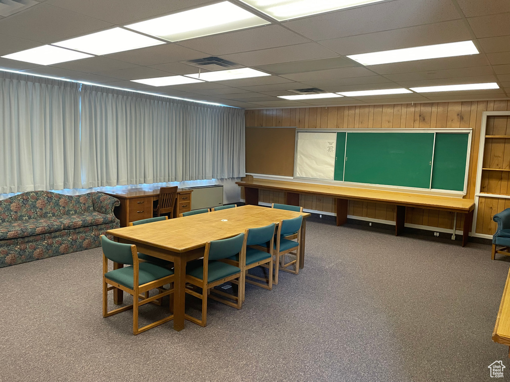 Carpeted dining area featuring a drop ceiling and wooden walls