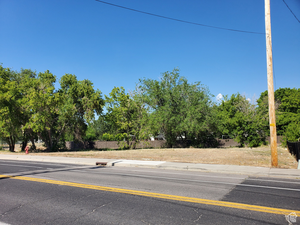 View of asphalt street featuring sidewalks, view of wooded area, and curbs