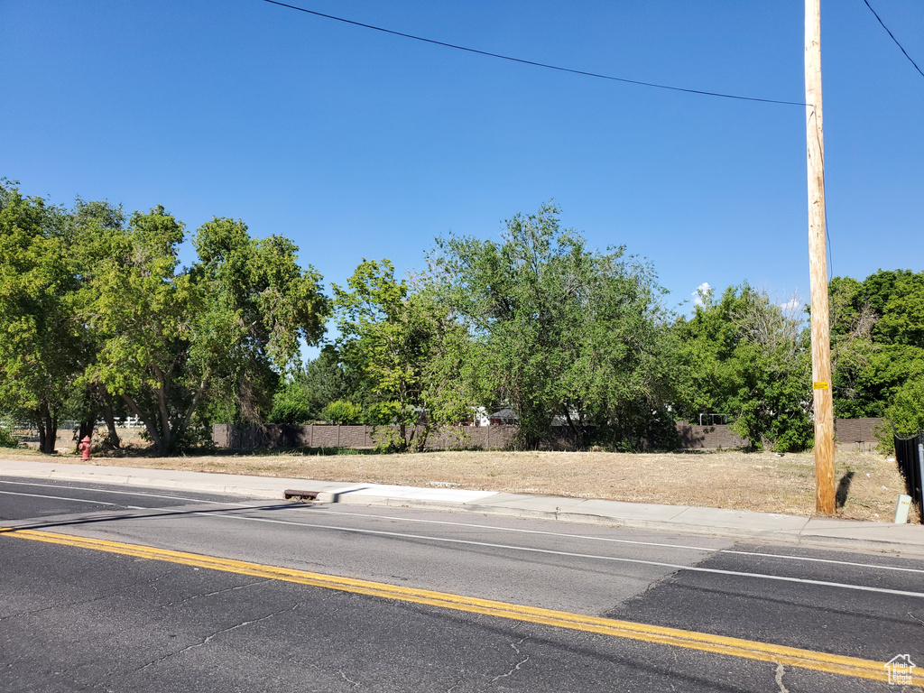 View of asphalt road featuring sidewalks, view of scattered trees, and curbs