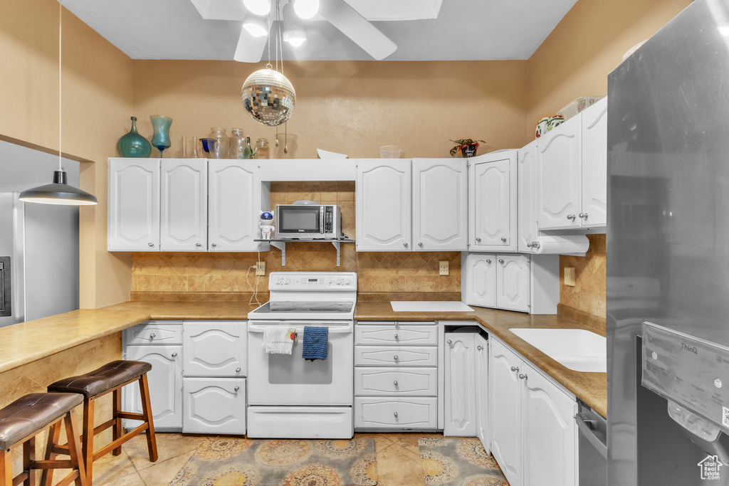 Kitchen featuring appliances with stainless steel finishes, ceiling fan, decorative backsplash, white cabinetry, and hanging light fixtures