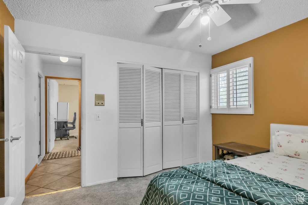 Tiled bedroom with a closet, carpet floors, a textured ceiling, a ceiling fan, and an office area