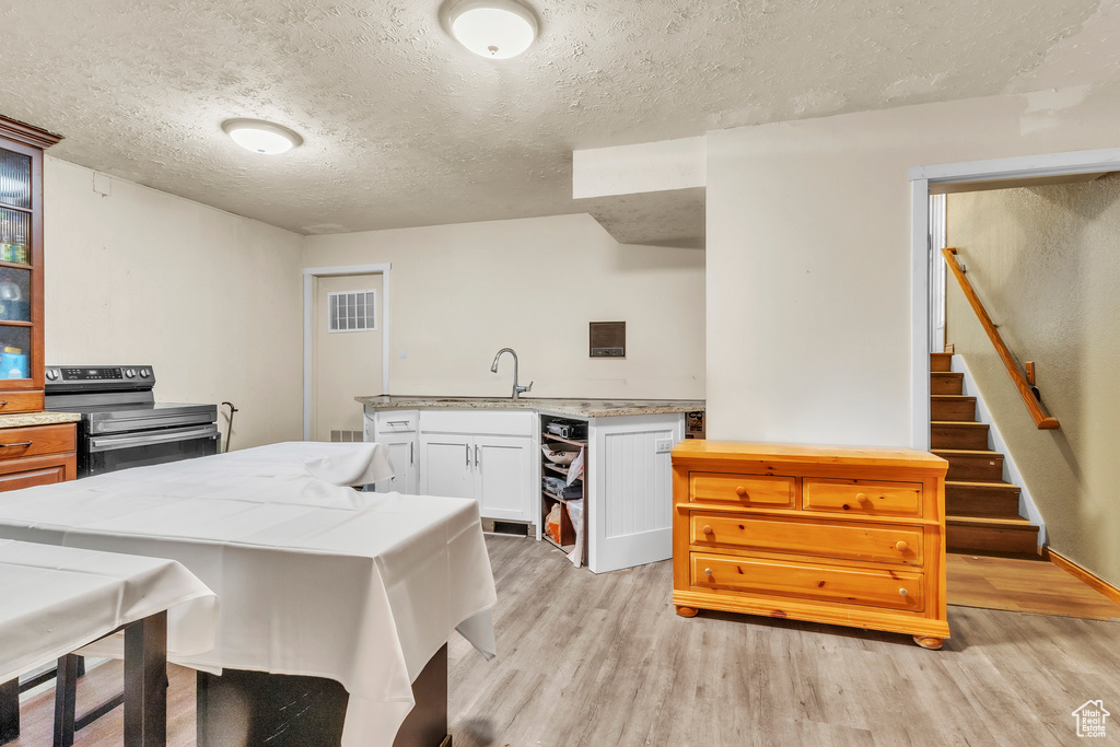 Kitchen with stainless steel electric range oven, a textured ceiling, light wood-style flooring, white cabinetry, and glass insert cabinets
