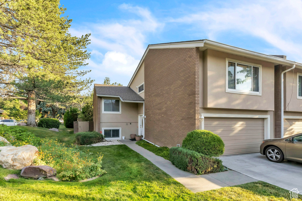 View of home\'s exterior with concrete driveway, a garage, stucco siding, a lawn, and brick siding