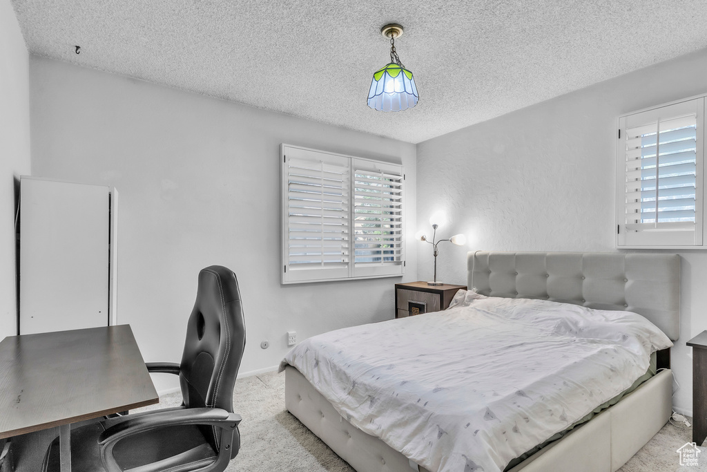 Bedroom featuring a textured ceiling, light colored carpet, and a desk