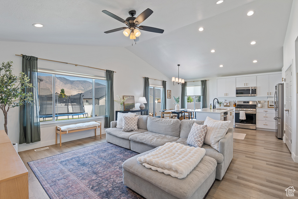 Living room featuring lofted ceiling, light wood-style flooring, recessed lighting, ceiling fan, and a chandelier
