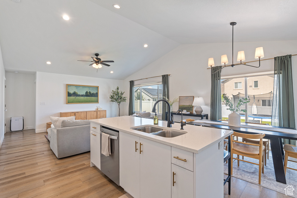 Kitchen featuring open floor plan, stainless steel dishwasher, light countertops, light wood-style floors, and vaulted ceiling