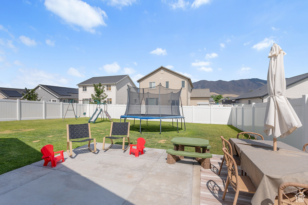 Fenced backyard with a trampoline, a patio area, a playground, and a residential view