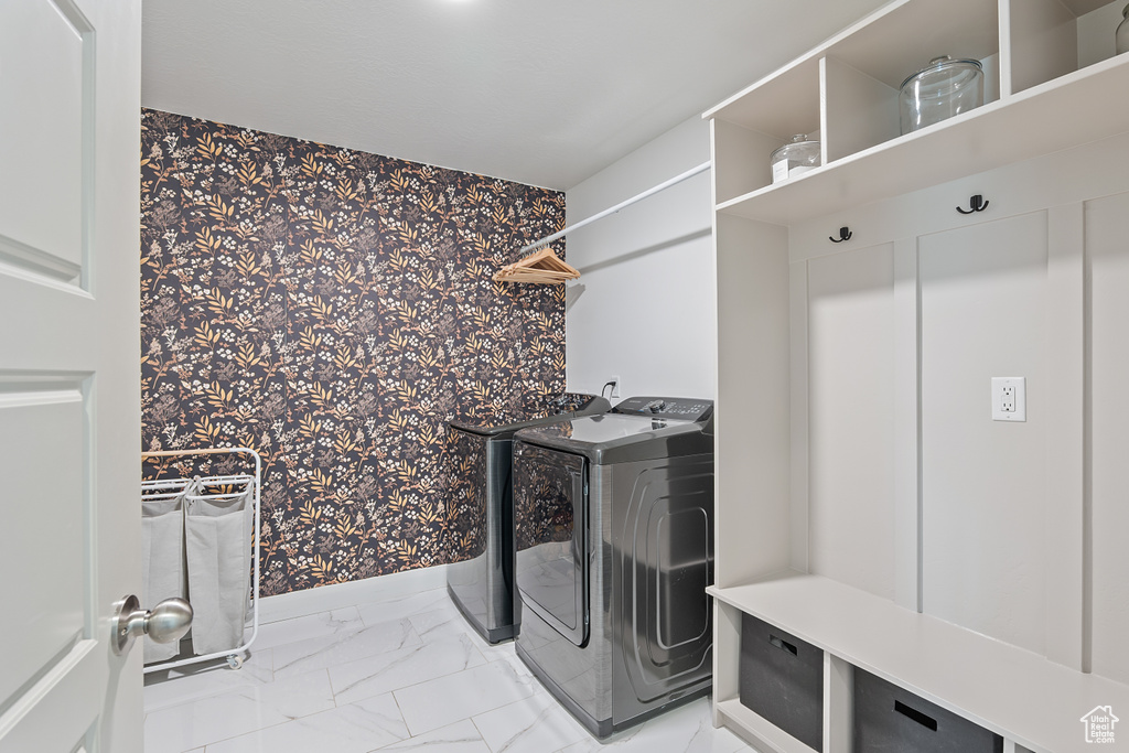 Laundry room featuring wallpapered walls, washer and clothes dryer, light marble finish floors, and an accent wall