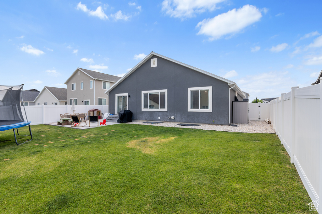 Back of house with a trampoline, a fenced backyard, a patio area, and stucco siding