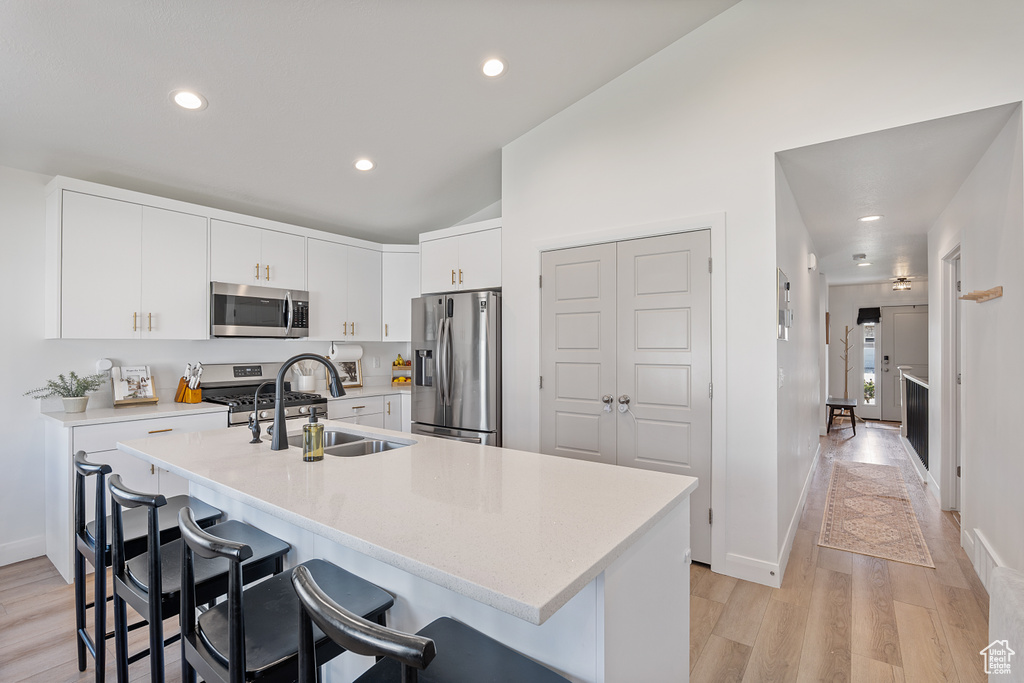 Kitchen with stainless steel appliances, a kitchen bar, light countertops, recessed lighting, and light wood-style flooring