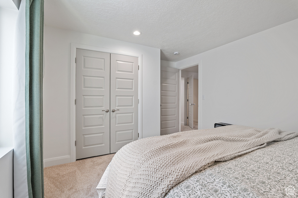 Bedroom with light colored carpet, a closet, recessed lighting, and a textured ceiling