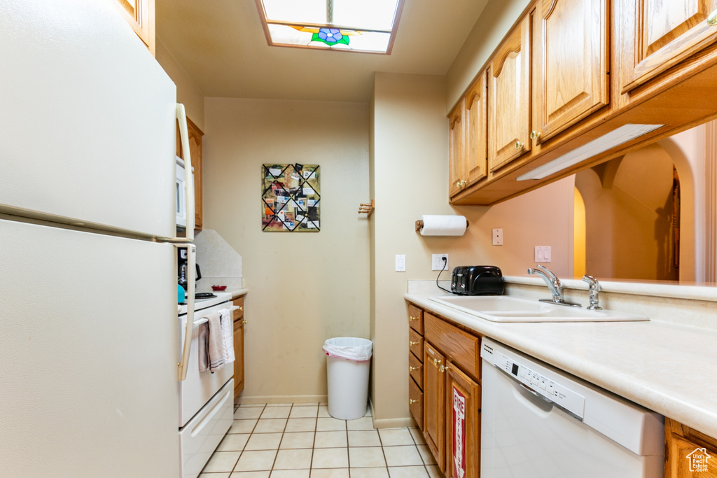 Kitchen featuring white appliances, light countertops, light tile patterned floors, and a skylight