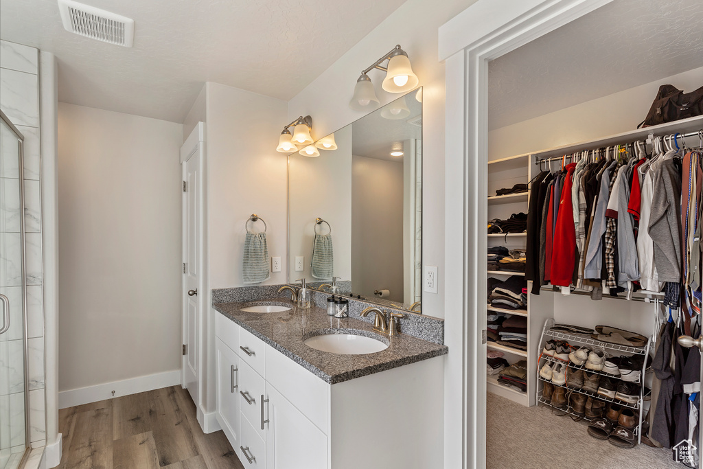 Bathroom featuring double vanity, a spacious closet, wood finished floors, and a tile shower