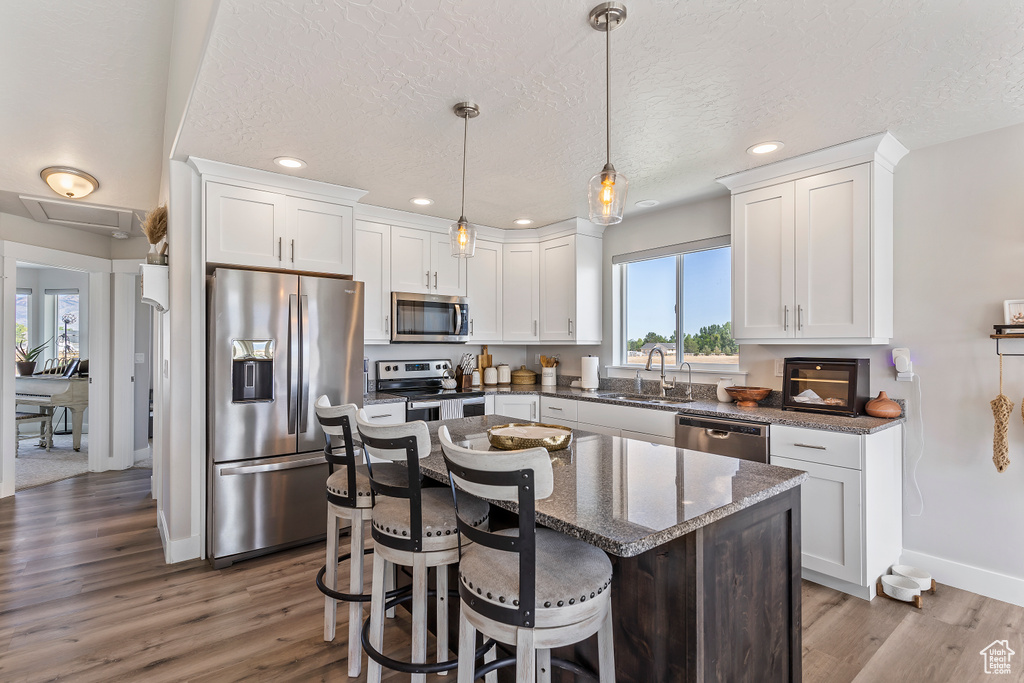Kitchen featuring stainless steel appliances, white cabinetry, wood finished floors, recessed lighting, and dark stone countertops