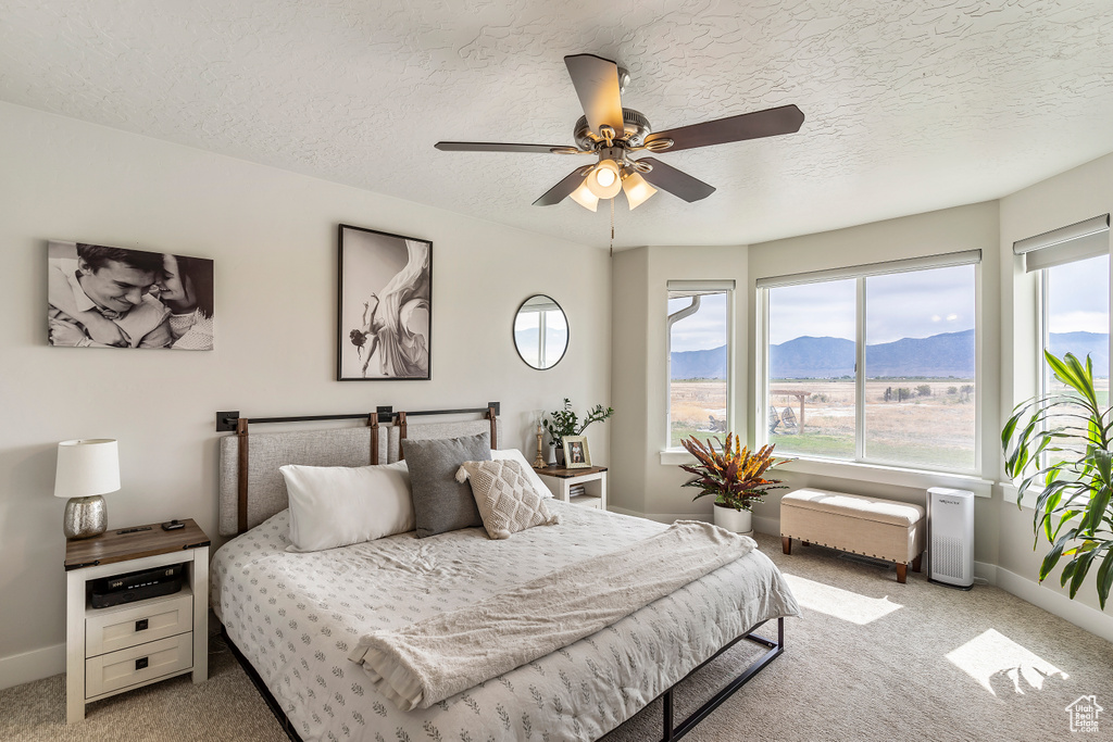 Bedroom with light colored carpet, multiple windows, a mountain view, a textured ceiling, and ceiling fan