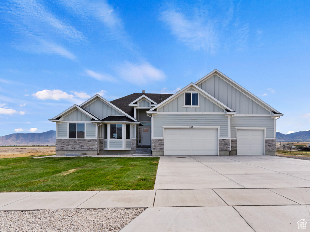 Craftsman-style home with a mountain view, board and batten siding, concrete driveway, stone siding, and a front yard