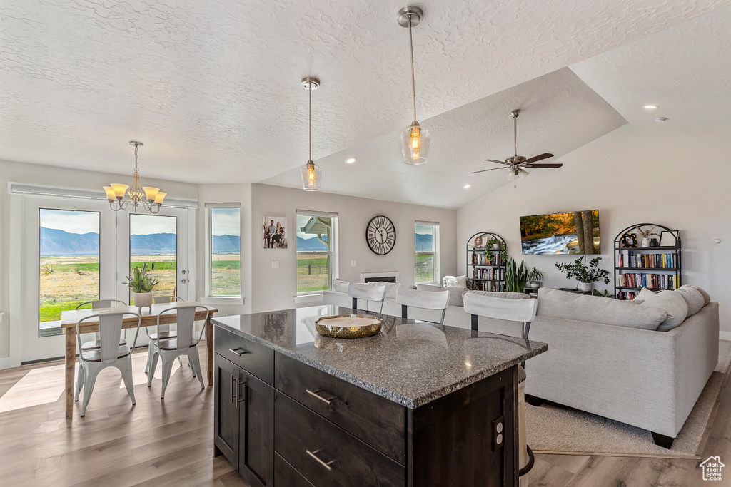 Kitchen with a textured ceiling, light wood finished floors, open floor plan, a chandelier, and decorative light fixtures