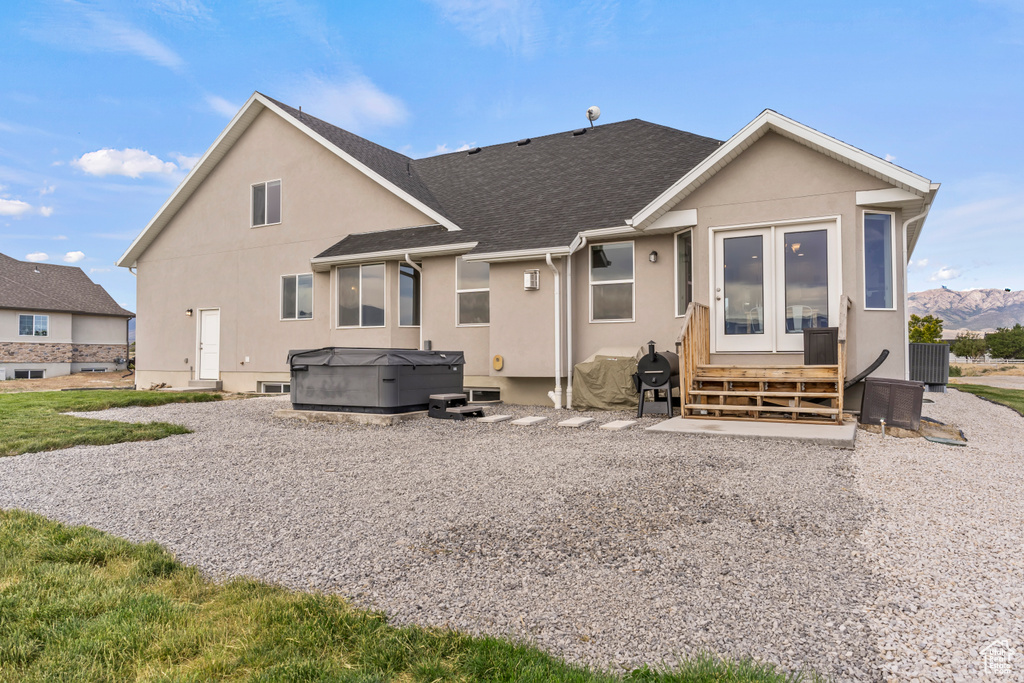 Rear view of house featuring a hot tub, stucco siding, and a shingled roof