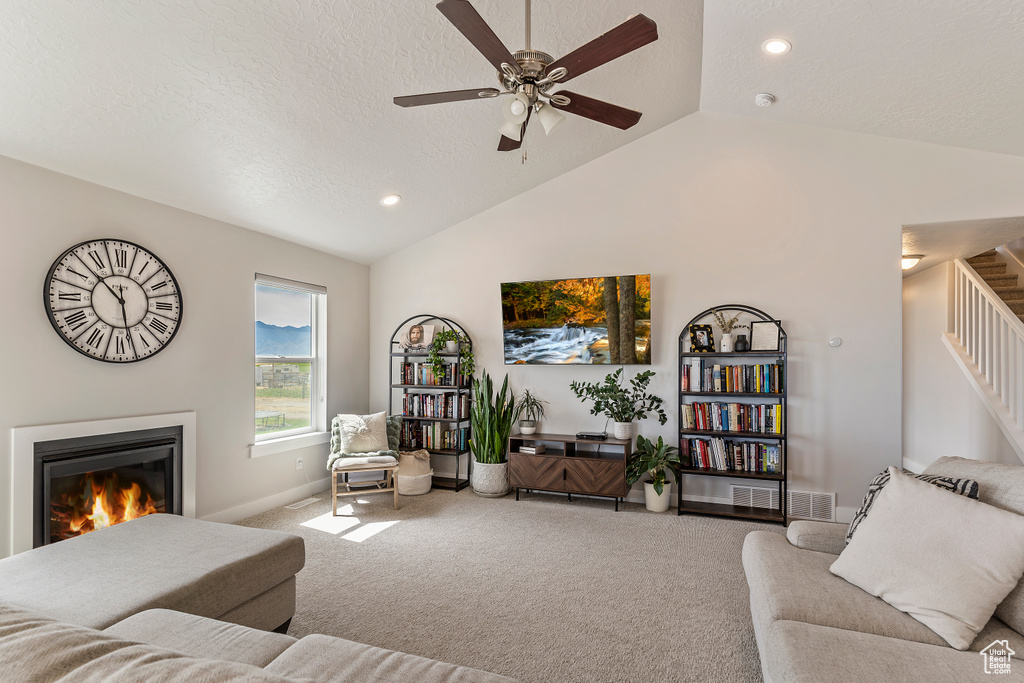 Living room featuring vaulted ceiling, carpet flooring, ceiling fan, a glass covered fireplace, and stairs
