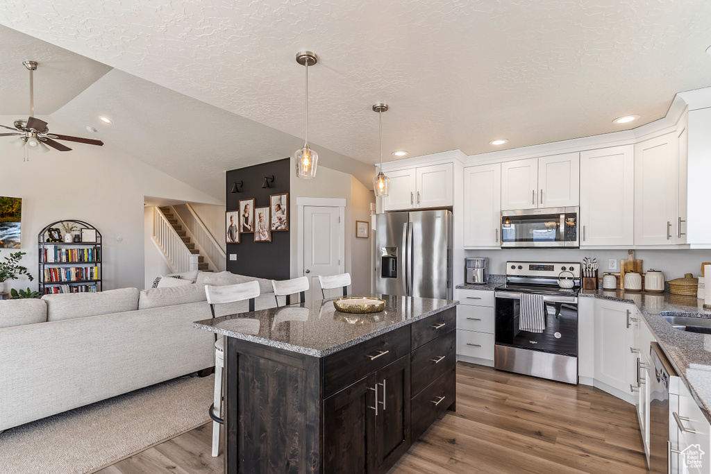 Kitchen with stainless steel appliances, open floor plan, a breakfast bar area, light wood-style flooring, and white cabinetry