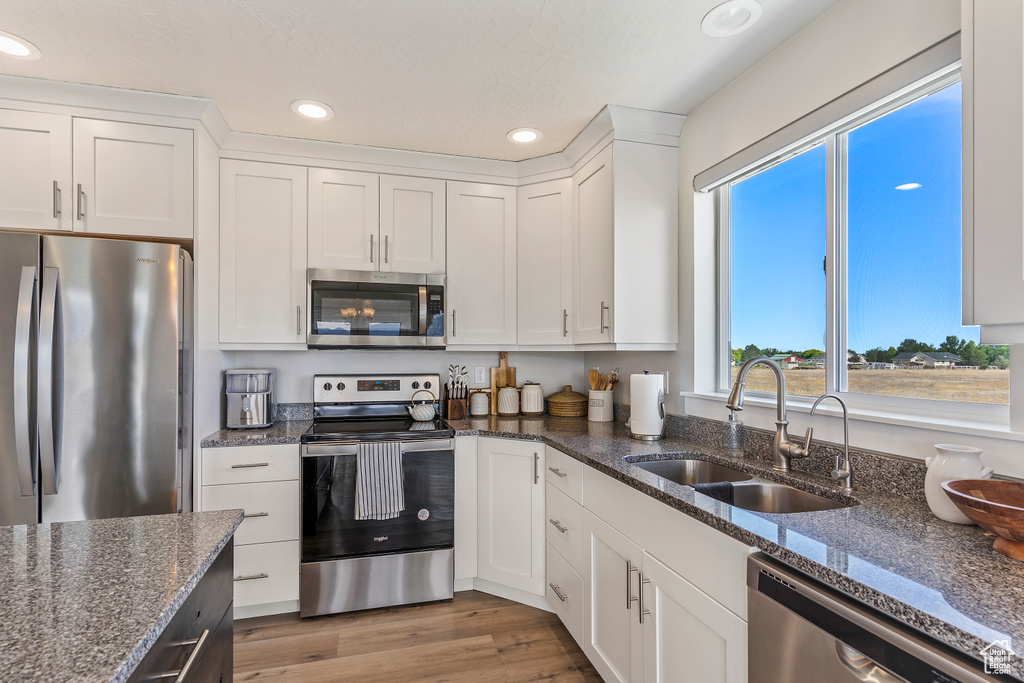 Kitchen with appliances with stainless steel finishes, white cabinetry, recessed lighting, light wood-type flooring, and dark stone countertops