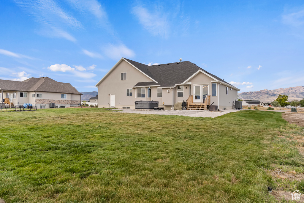 Back of house featuring a hot tub, a mountain view, a patio area, a lawn, and entry steps